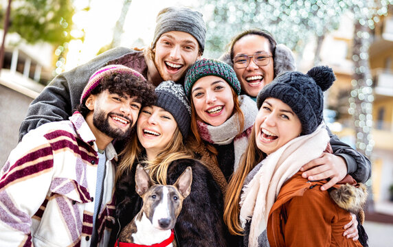 Happy multicultural guys and girls taking selfie on warm fashion clothes - Trendy life style concept with millenial friends group having fun together out side on winter holidays - Bright vivid filter