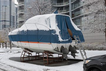 The motorboat is covered with a cover and stands outdoors in the snow. Preparing the boat for winter