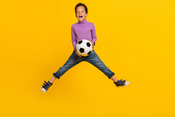 Full size photo of overjoyed energetic boy jumping hands hold football isolated on yellow color background