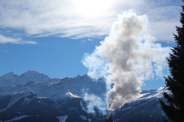 Steam coming from a smokestack seen in a mountain landscape. Snow covered mountains