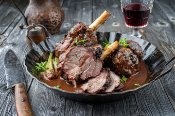 Traditional Greek barbecue lamb knuckles in red wine sauce serve as close-up in a rustic casserole