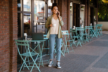 Hispanic woman drinking coffee and talking on mobile phone at cafe