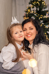 mother and daughter are hugging each other behind the Christmas tree