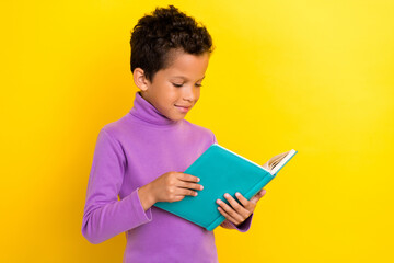 Portrait of intelligent schoolkid arms hold book reading isolated on yellow color background