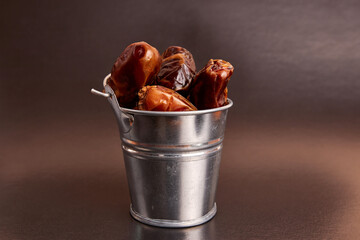 A small metal bucket filled with dried dates on a brown background.