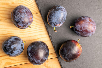 Several organic black plums on a slate board, close-up, on a wooden table, top view.