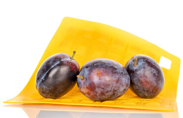 Three organic plums on a yellow silicone napkin, close-up, isolated on a white background.