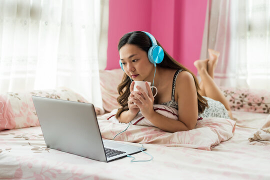 Asian young woman on bed watch online movie and drink coffee