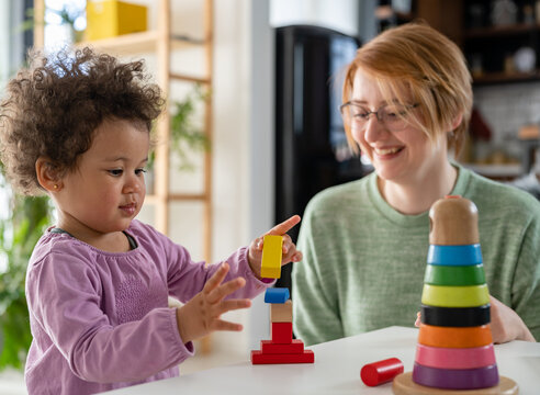 Mother looking at a child playing with an educational didactic toy. Young woman and child playing with didactic toys