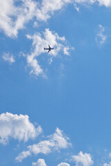 The passenger plane is flying far away in the blue sky and white clouds. Airplane in the air. International passenger air transportation. The plane flies in the distance. Vertical illustration
