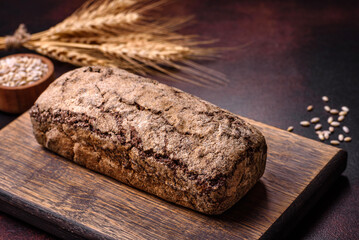 A loaf of brown bread with grains of cereals on a wooden cutting board