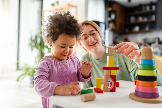 Mother looking at a child playing with an educational didactic toy. Young woman and child playing with didactic toys