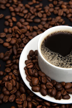 Vertical image of a cup of coffee and coffee beans scattered around