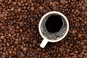 Strong coffee in a foam mug surrounded by coffee beans