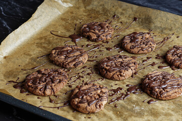 Topping with chocolate threads over cookies on a baking sheet.