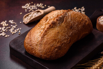 A loaf of brown bread with grains of cereals on a wooden cutting board