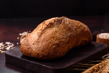 A loaf of brown bread with grains of cereals on a wooden cutting board