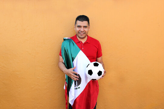 Mexican adult man plays with a soccer ball very excited that he is going to see the game with de mexican flag and wants to see his team win