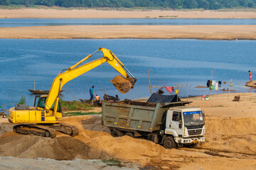 excavator at work site loading sand on dumper at the bank of a reaver.