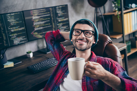 Photo of smart dreamy programmer wear spectacles arm behind head having coffee break indoors workplace workshop home