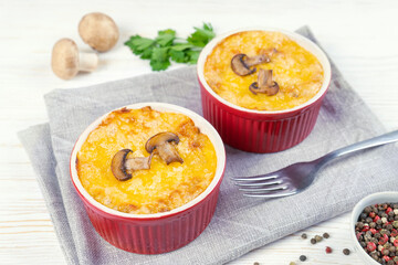 Chicken and mushroom casserole with golden crust, julienne with baked cheese, creamy gratin in portion ramekin clay pot on white wooden background. French cuisine. Top view, flat lay with copy space