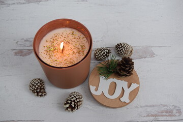 Holiday wood wick candle with pine cones and the word joy on wooden lid. 