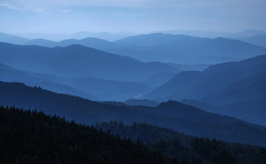 Plakat High peaks of beautiful dark blue mountain range landscape with fog and forest. Horizontal image.