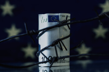 Economic warfare, sanctions and embargo busting concept. EU money wrapped in barbed wire against flag of European Union.