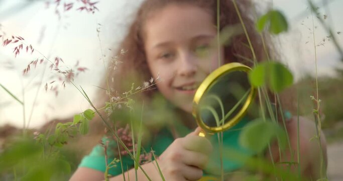 Child is playing on the grass in park. Happy cute little girl, Smile of Child and look up to camera. 4K. Portrait happy smiling funny child looking at camera playing with magnifying glass.