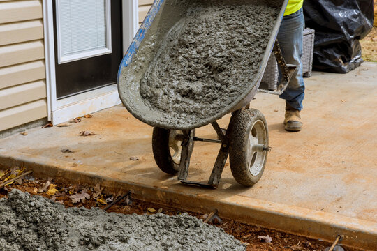 Making new concrete sidewalk path near house with wet cement concreting with worker using wheelbarrow