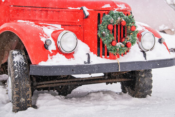 Red vintage car decorated with christmas wreath snowy winter outside.