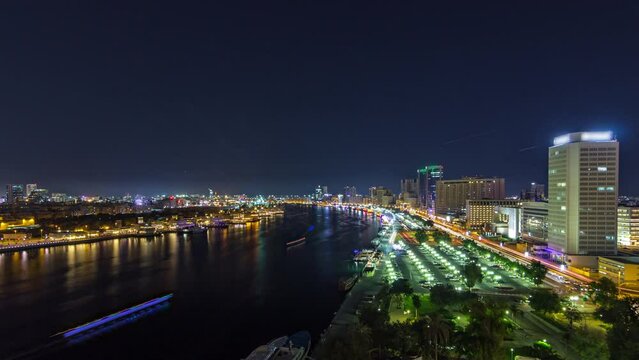Dubai creek panoramic landscape day to night transition timelapse with boats and yachts and modern buildings with traffic on the road and car parking. Aerial top view from above