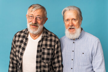 Portrait two elderly man friends standing over blue background - friendship, aged and senior people