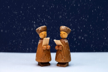 Wooden cute carol singers figurines closeup on holly night at Christmas with snow falling
