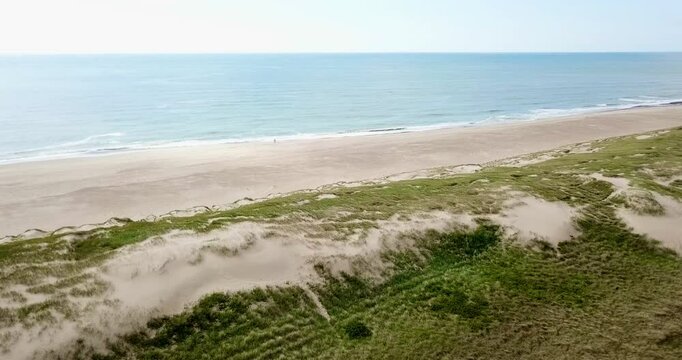 flying from sandy dunes over an almost empty beach with two persons to the ocean, North Sea, Denmark, tourism, nature, high quality video