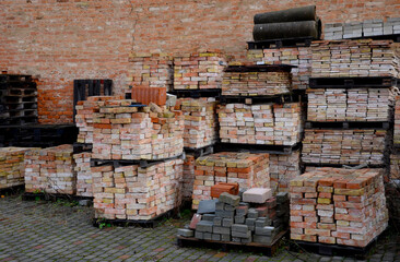 in the yard of the brickyard, by the wall, there is a warehouse of pallets with stacked products, they will not be buried by people. reconstruction of an old house made of burnt tiles