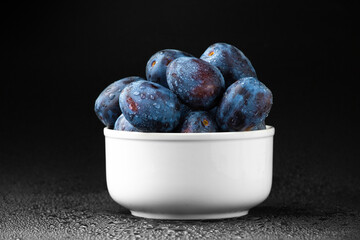 A handful of blue plums in a white plate on a dark background.