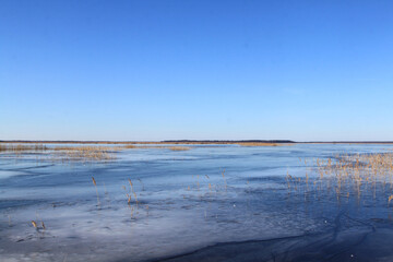 Earlier spring scenery with lake covered with a bit of ice and clear blue sky