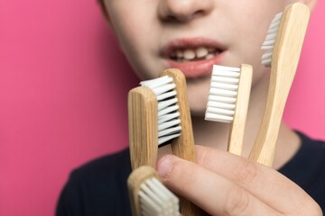 a boy of European appearance holds bamboo toothbrushes in his hands. Eco friendly. close-up photo of a child's smile