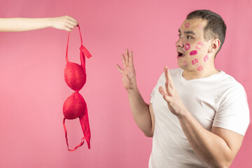 A woman's hand with a red bra and a man with traces of a kiss on his face in anticipation of sex, pink background. The concept of sex,sexual relations,love,sexual foreplay