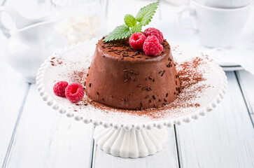 Traditional Italian chocolate pudding with raspberry and chocolate crumbles served as close-up on a classic cake plate