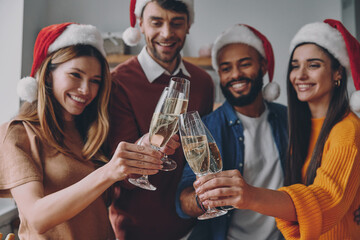 Group of beautiful young people in Christmas hats toasting with champagne and smiling