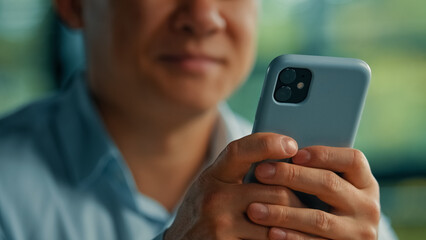 Unknown asian man businessman worker modern user senior entrepreneur hold in hands phone search online information use mobile business apps wifi 5g connection in office texting messages on smartphone