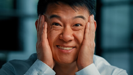 Positive emotional asian korean man businessman 40s male employee hold face by hands feel happiness triumph good shock opens mouth with delight wow reaction professional success career growth victory