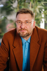 Waist up portrait of bearded gaffer sitting on chair and looking at camera. He is wearing a glasses.