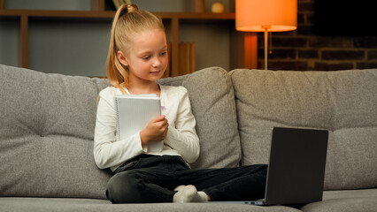 Happy caucasian preteen girl pupil little child sit in cozy pose on sofa distance learning online...