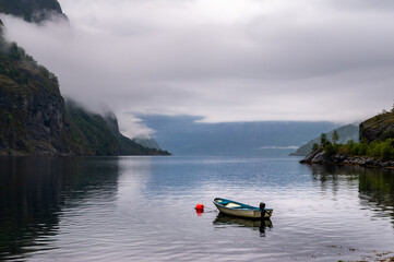 Personal boat anchored in fjord water in Aurlandfjord by Flam in Norway with rain clouds covering the mountains in the background