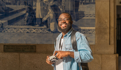 Smiling young african american man with cmera against classical azulejo wall. Travel in Portugal