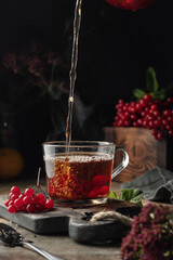 Viburnum tea is poured into a cup with steam, pouring process. Autumn seasonal healthy drink. Dark...
