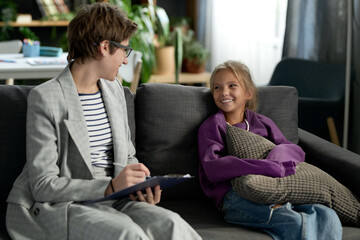 Social worker making notes and having positive conversation with little girl while they sitting on...